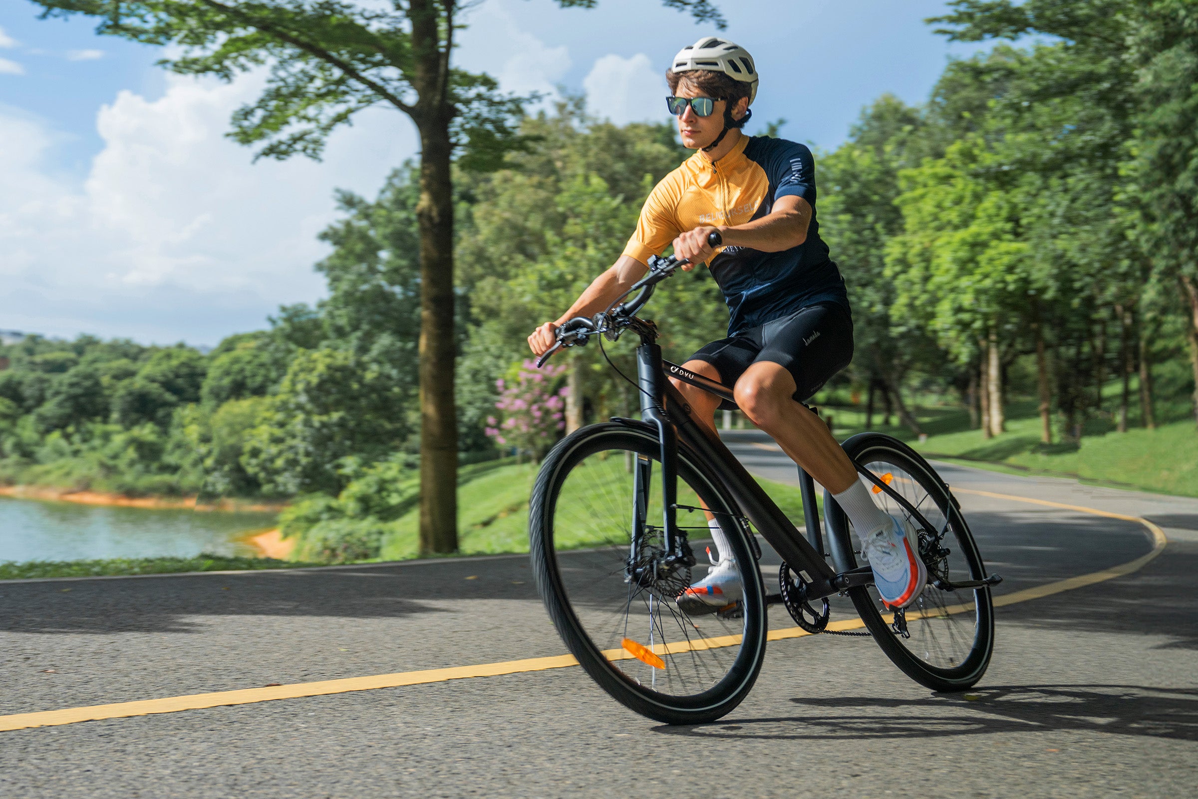 Homme pédalant sur un vélo électrique noir sur route près d'un lac. Homme pédalant sur un vélo électrique noir sur route près d'un lac.