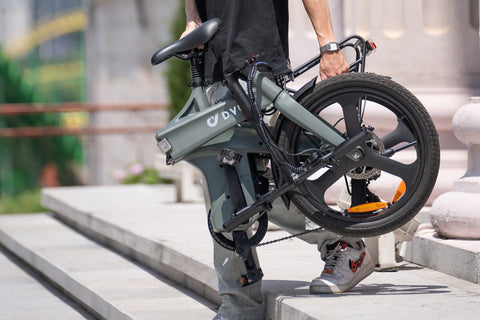 Homme transportant le vélo électrique DYU T1 pliable gris à la main. Homme transportant le vélo électrique DYU T1 pliable gris à la main.