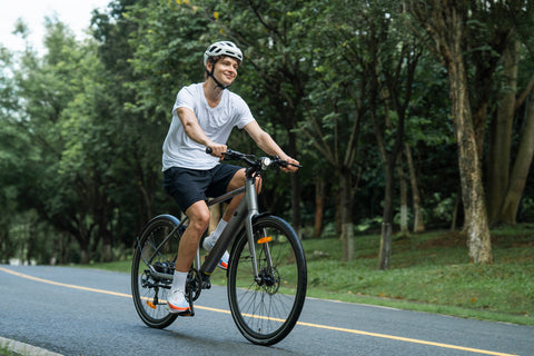 Homme souriant sur un vélo électrique gris sur route boisée, idéal pour les trajets urbains. Homme souriant sur un vélo électrique gris sur route boisée, idéal pour les trajets urbains.