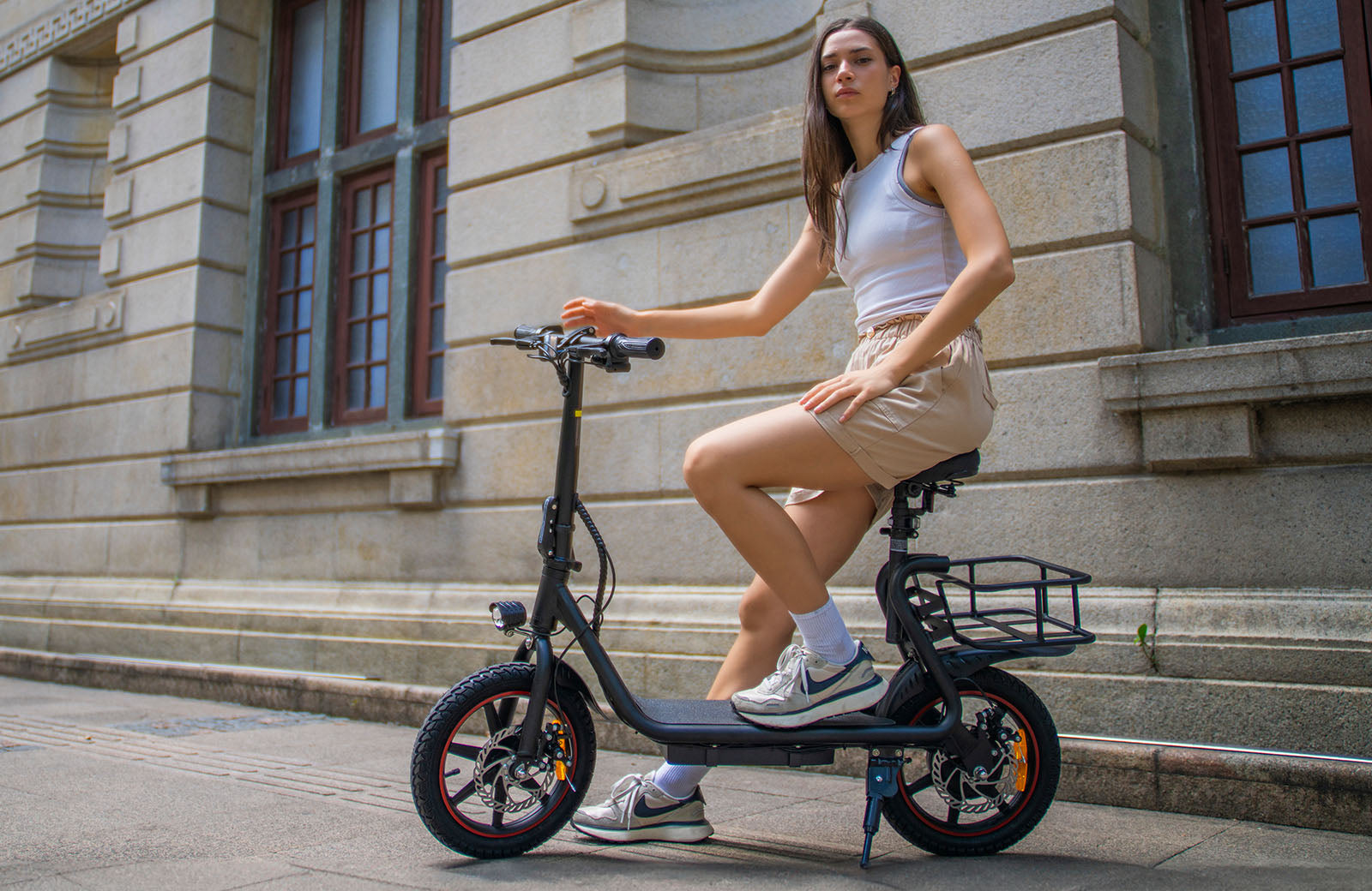 Femme en short sur DYU C4 noir, vélo électrique avec panier arrière en milieu urbain Femme en short sur DYU C4 noir, vélo électrique avec panier arrière en milieu urbain