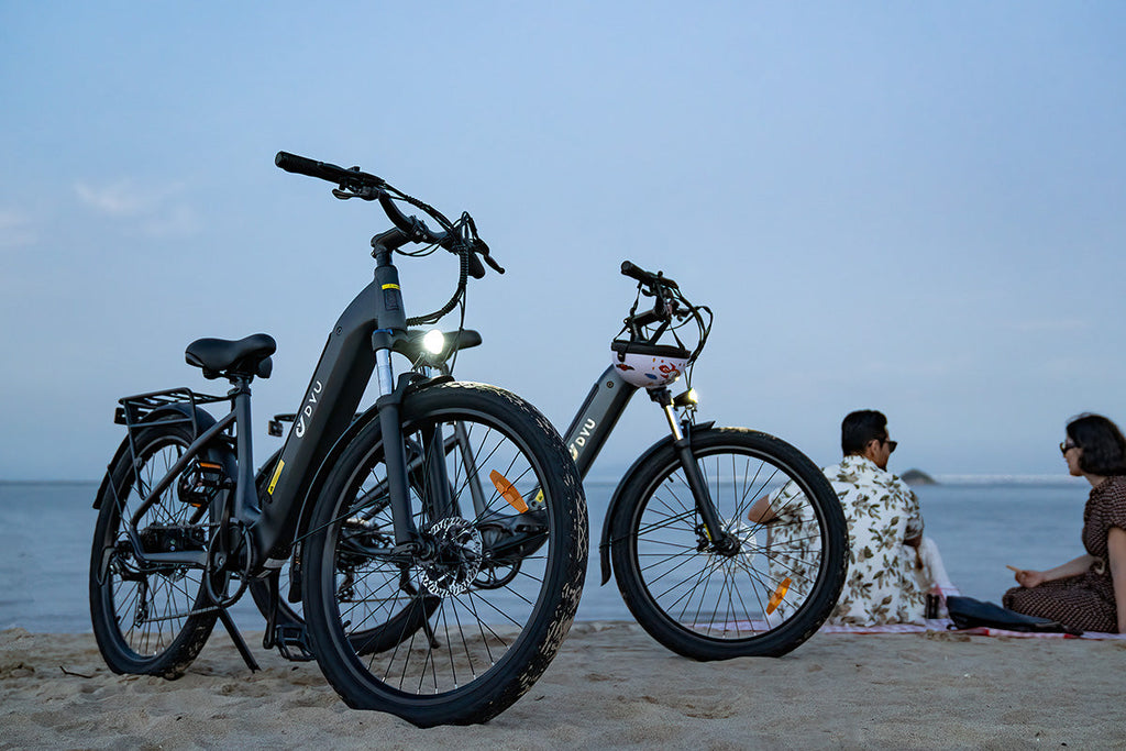 Vélos électriques DYU C1 noir et gris sur la plage, décor relaxant au bord de la mer.